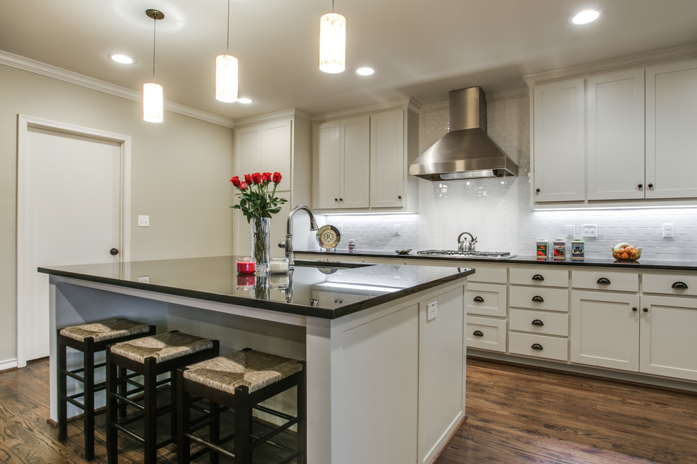 Design ideas for a mid-sized traditional single-wall open plan kitchen in Dallas with an undermount sink, shaker cabinets, white cabinets, granite benchtops, white splashback, ceramic splashback, stainless steel appliances, medium hardwood floors and with island.