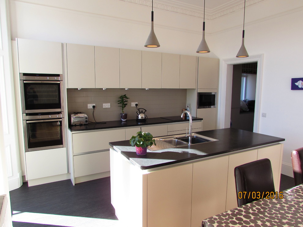 Design ideas for a mid-sized modern single-wall eat-in kitchen in Edinburgh with an undermount sink, flat-panel cabinets, beige cabinets, solid surface benchtops, grey splashback, porcelain splashback, stainless steel appliances, vinyl floors and with island.