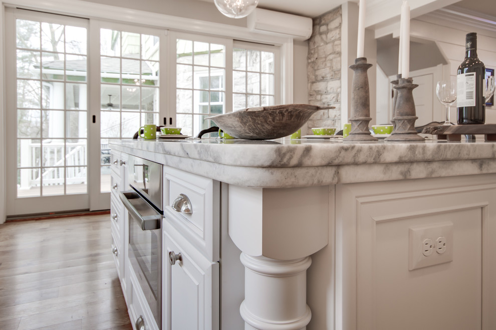 Inspiration for a large traditional l-shaped eat-in kitchen in Philadelphia with a farmhouse sink, beaded inset cabinets, white cabinets, quartzite benchtops, white splashback, stone tile splashback, black appliances, medium hardwood floors and with island.