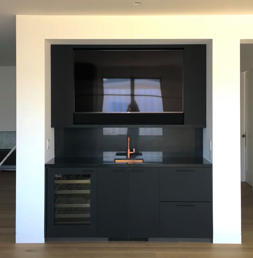 Design ideas for a small modern single-wall wet bar in San Diego with flat-panel cabinets, black cabinets, marble benchtops, black splashback, marble splashback, light hardwood floors, brown floor, black benchtop and an undermount sink.