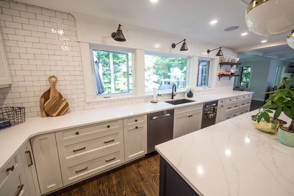 Design ideas for a large transitional u-shaped eat-in kitchen in Toronto with an undermount sink, shaker cabinets, white cabinets, solid surface benchtops, white splashback, subway tile splashback, stainless steel appliances, medium hardwood floors, multiple islands and brown floor.