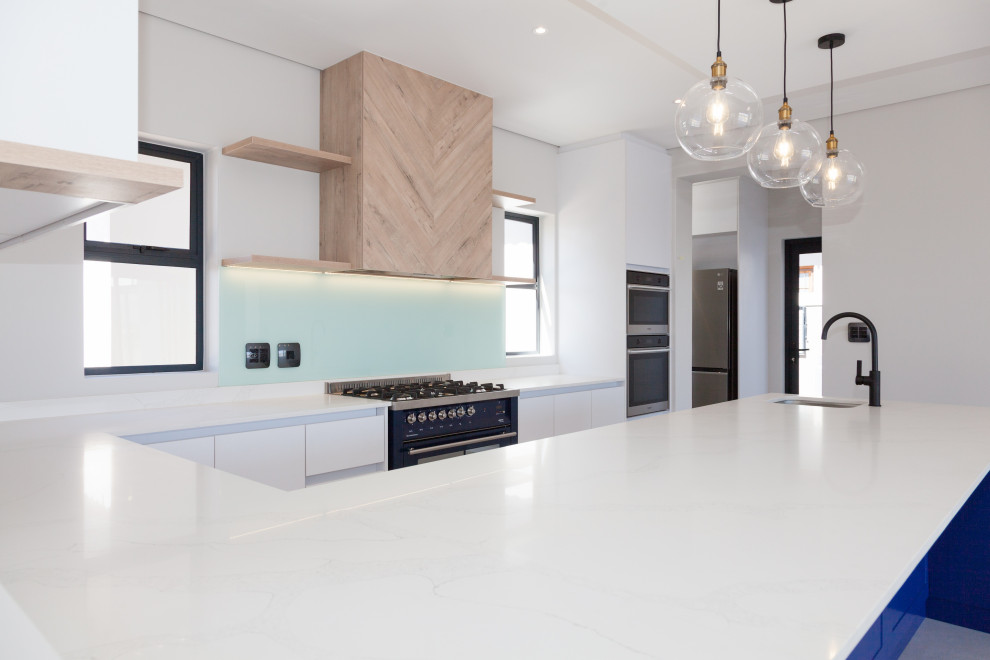 Eat-in kitchen - u-shaped eat-in kitchen idea with an undermount sink, flat-panel cabinets, white cabinets, quartz countertops, blue backsplash, glass tile backsplash, colored appliances, an island and white countertops