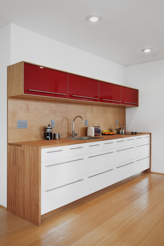 Inspiration for a mid-sized midcentury single-wall kitchen in Seattle with a drop-in sink, flat-panel cabinets, white cabinets, wood benchtops, brown splashback and medium hardwood floors.