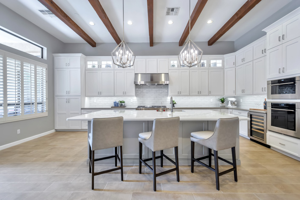 Eat-in kitchen - large transitional l-shaped porcelain tile and brown floor eat-in kitchen idea in Phoenix with a farmhouse sink, shaker cabinets, white cabinets, quartz countertops, white backsplash, subway tile backsplash, stainless steel appliances, an island and gray countertops