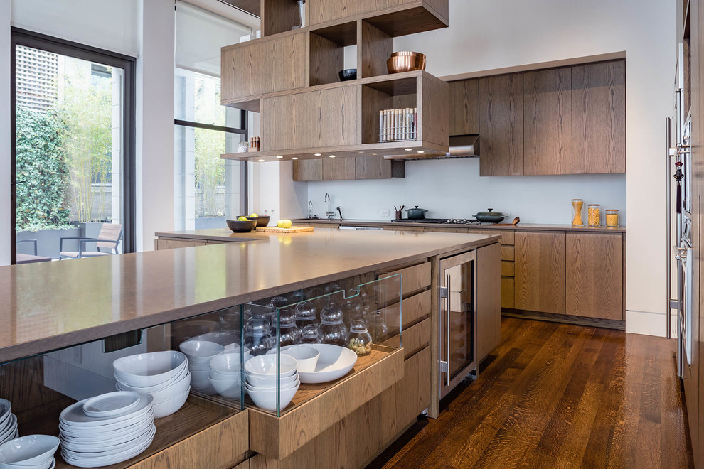 Large contemporary kitchen in New York with a double-bowl sink, flat-panel cabinets, medium wood cabinets, quartz benchtops, white splashback, glass sheet splashback, stainless steel appliances, medium hardwood floors, with island, brown floor and beige benchtop.