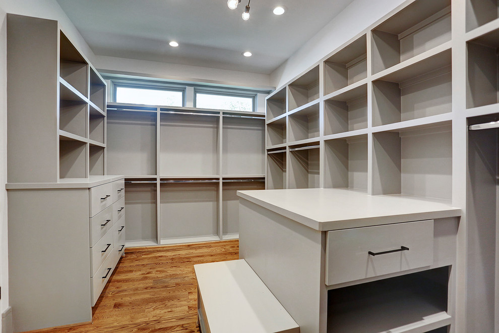 This is an example of a large contemporary gender-neutral walk-in wardrobe with flat-panel cabinets, grey cabinets, medium hardwood floors and brown floor.