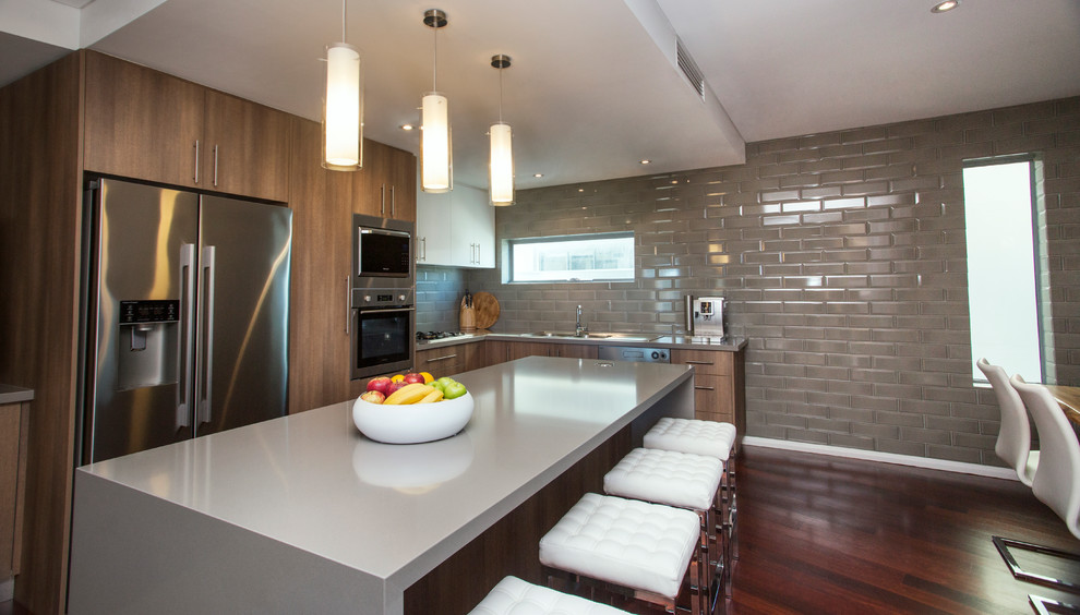 This is an example of a mid-sized contemporary l-shaped open plan kitchen in Perth with a double-bowl sink, flat-panel cabinets, medium wood cabinets, quartz benchtops, grey splashback, ceramic splashback, stainless steel appliances, dark hardwood floors, with island and red floor.