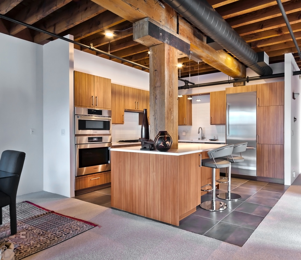 Photo of a mid-sized industrial l-shaped eat-in kitchen in Minneapolis with an undermount sink, flat-panel cabinets, medium wood cabinets, quartz benchtops, white splashback, glass tile splashback, stainless steel appliances, porcelain floors and with island.