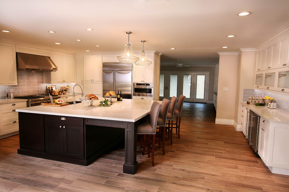 Inspiration for a large transitional u-shaped light wood floor kitchen pantry remodel with a farmhouse sink, shaker cabinets, white cabinets, quartz countertops, gray backsplash, glass tile backsplash, stainless steel appliances and an island