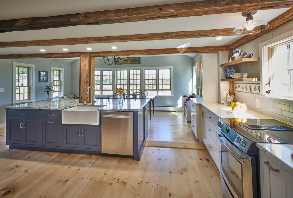 This is an example of a rural kitchen/diner in Boston with a belfast sink, shaker cabinets, white cabinets, engineered stone countertops, white splashback, metro tiled splashback, stainless steel appliances, light hardwood flooring, an island, brown floors, blue worktops and exposed beams.