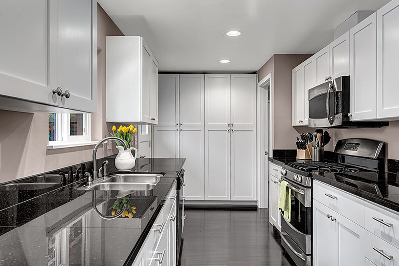 Inspiration for a small modern galley kitchen pantry in Seattle with an undermount sink, shaker cabinets, white cabinets, granite benchtops, black splashback, stone tile splashback, stainless steel appliances and dark hardwood floors.