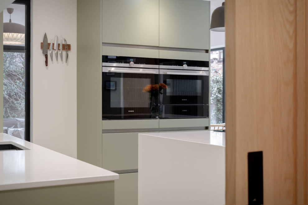 Medium sized contemporary l-shaped open plan kitchen in Other with a built-in sink, flat-panel cabinets, grey cabinets, quartz worktops, mirror splashback, black appliances, an island and white worktops.