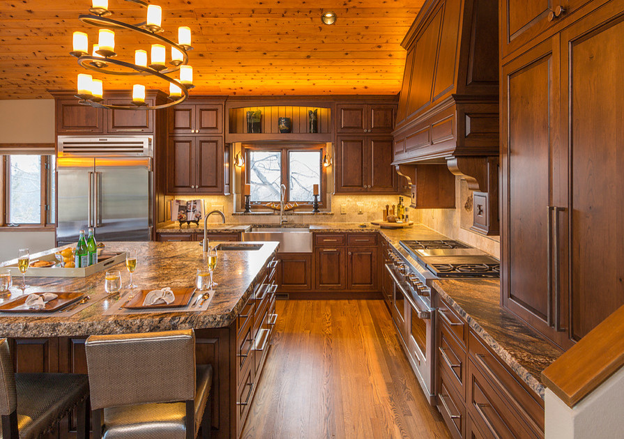 Eat-in kitchen - mid-sized rustic l-shaped light wood floor eat-in kitchen idea in Denver with a farmhouse sink, raised-panel cabinets, dark wood cabinets, granite countertops, beige backsplash, porcelain backsplash, stainless steel appliances and an island