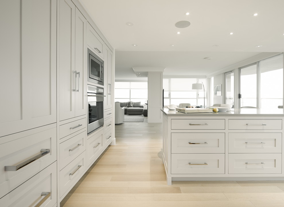 Inspiration for a mid-sized transitional u-shaped eat-in kitchen in Vancouver with an undermount sink, shaker cabinets, grey cabinets, quartz benchtops, white splashback, ceramic splashback, stainless steel appliances, light hardwood floors and with island.