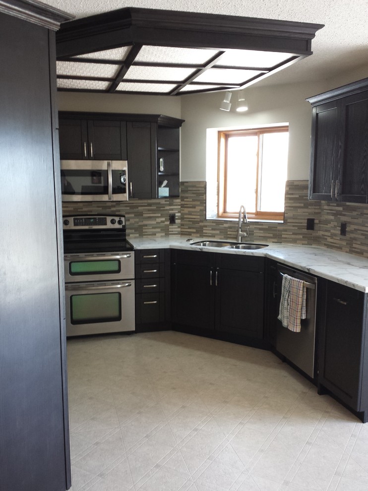 Example of a mid-sized transitional u-shaped ceramic tile and beige floor enclosed kitchen design in Calgary with an undermount sink, shaker cabinets, stainless steel appliances, black cabinets, marble countertops, beige backsplash, matchstick tile backsplash and no island