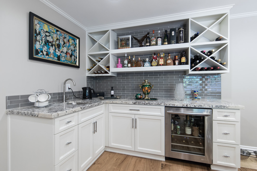 Inspiration for a mid-sized transitional l-shaped wet bar in Los Angeles with an undermount sink, recessed-panel cabinets, white cabinets, grey splashback, glass tile splashback, medium hardwood floors, brown floor, grey benchtop and granite benchtops.