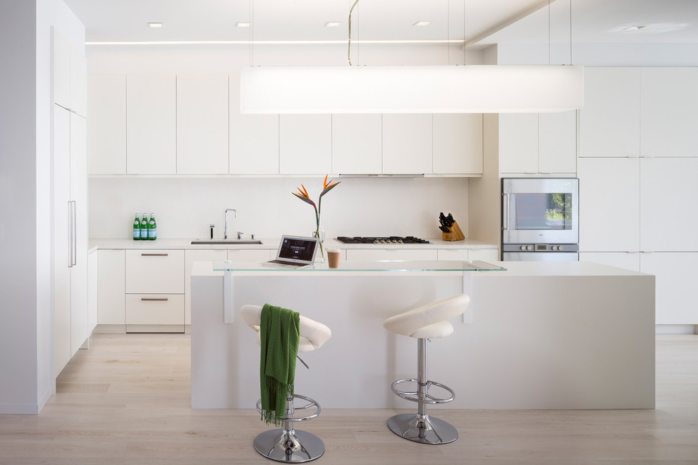 Photo of a large contemporary l-shaped open plan kitchen in San Francisco with an undermount sink, flat-panel cabinets, white cabinets, quartz benchtops, white splashback, panelled appliances, light hardwood floors and with island.