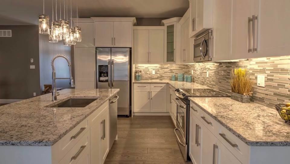 Example of a mid-sized transitional l-shaped medium tone wood floor and brown floor open concept kitchen design with an undermount sink, shaker cabinets, white cabinets, granite countertops, gray backsplash, matchstick tile backsplash, stainless steel appliances, an island and gray countertops