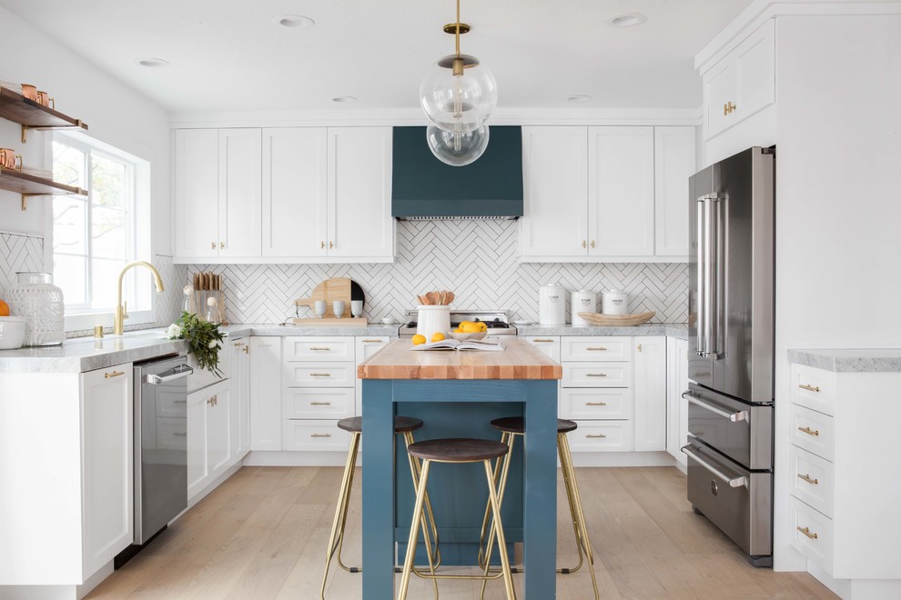 Mid-sized transitional u-shaped open plan kitchen in Orange County with a farmhouse sink, white cabinets, marble benchtops, white splashback, ceramic splashback, light hardwood floors, with island, shaker cabinets, stainless steel appliances and beige floor.
