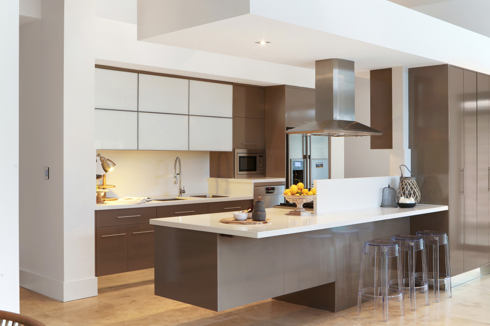 This is an example of a contemporary galley kitchen in Central Coast with an undermount sink, flat-panel cabinets, brown cabinets, stainless steel appliances, with island, beige floor and white benchtop.