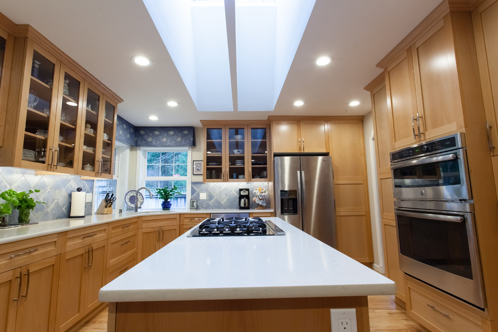 This is an example of a mid-sized traditional l-shaped separate kitchen in Seattle with shaker cabinets, light wood cabinets, quartz benchtops, blue splashback, stone tile splashback, stainless steel appliances, light hardwood floors, with island, beige floor and beige benchtop.