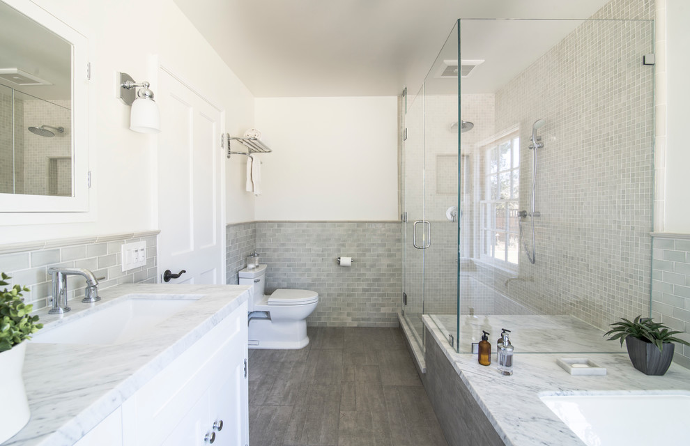 Photo of a traditional bathroom in Los Angeles with shaker cabinets, white cabinets, an undermount tub, a corner shower, a two-piece toilet, gray tile and white walls.