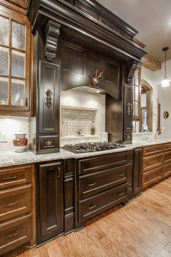 This is an example of a large country u-shaped eat-in kitchen in Dallas with glass-front cabinets, medium wood cabinets, granite benchtops, stone tile splashback, stainless steel appliances, medium hardwood floors, with island and brown floor.