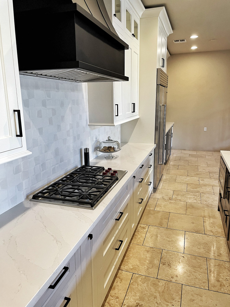 This is an example of an expansive transitional l-shaped eat-in kitchen in Phoenix with an undermount sink, shaker cabinets, white cabinets, quartz benchtops, white splashback, ceramic splashback, stainless steel appliances, travertine floors, with island, beige floor, white benchtop and vaulted.