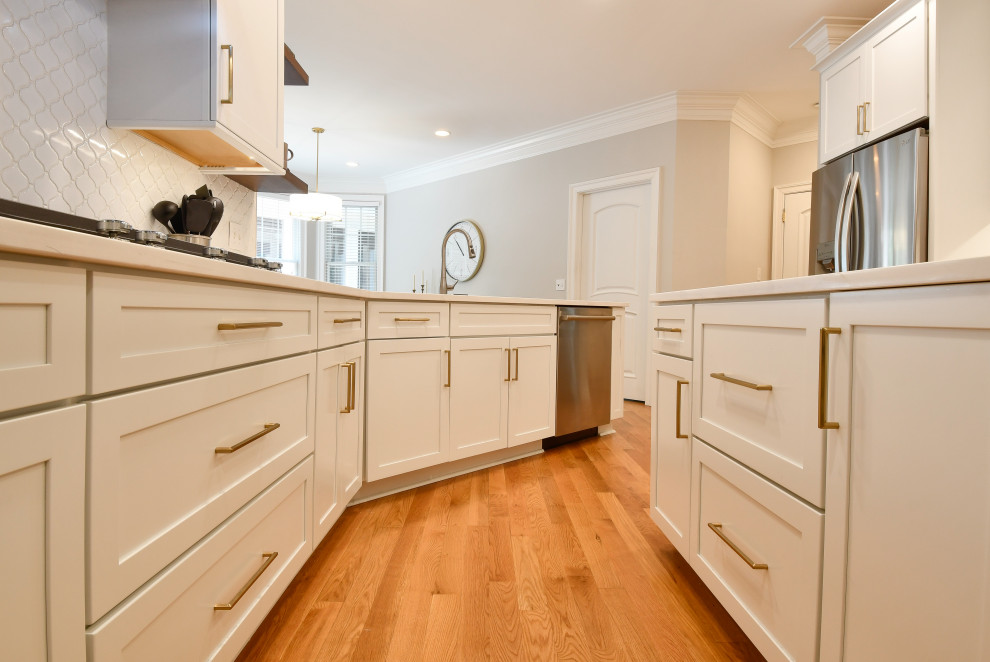 This is an example of an expansive transitional u-shaped open plan kitchen in DC Metro with a drop-in sink, recessed-panel cabinets, white cabinets, quartz benchtops, mosaic tile splashback, stainless steel appliances, with island and white benchtop.