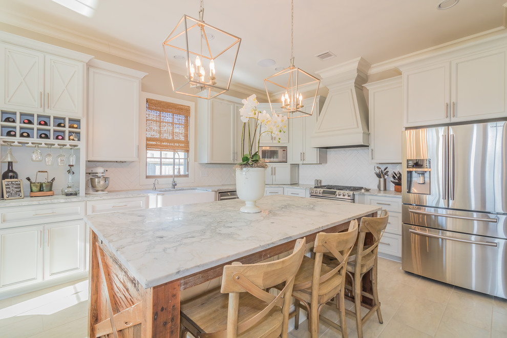 Photo of a country l-shaped kitchen in New Orleans with a farmhouse sink, recessed-panel cabinets, white cabinets, white splashback, stainless steel appliances, with island and white floor.