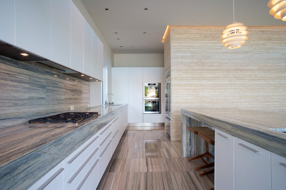 Contemporary galley kitchen in Miami with flat-panel cabinets, white cabinets, stone slab splashback, stainless steel appliances, marble benchtops and beige splashback.