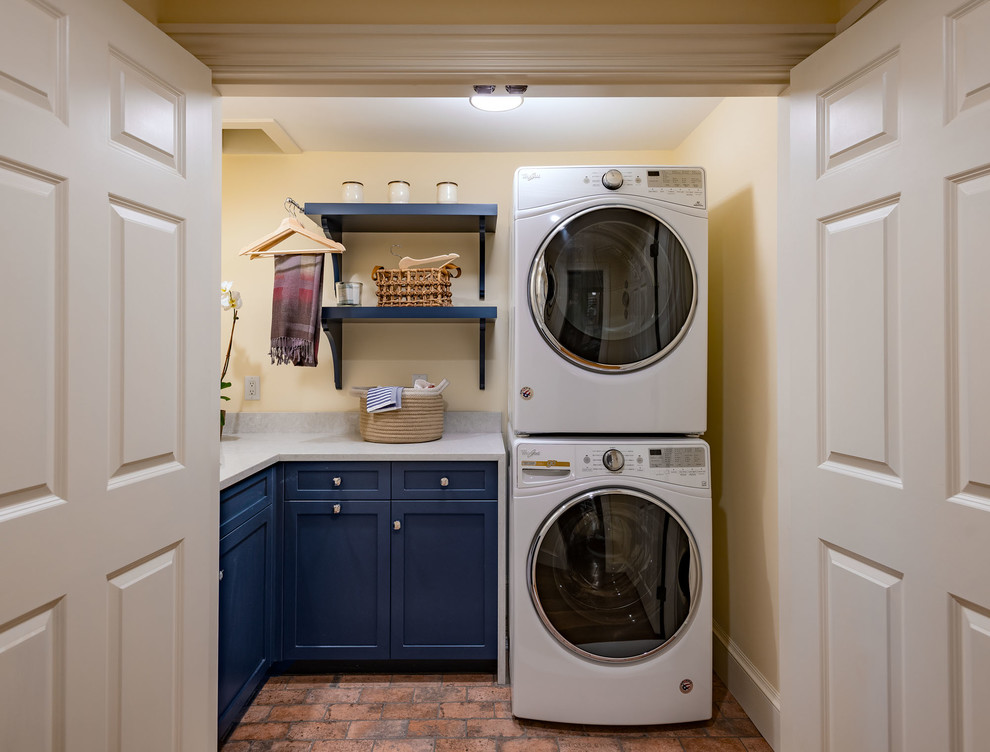 Design ideas for a small traditional l-shaped dedicated laundry room in Boston with an undermount sink, recessed-panel cabinets, blue cabinets, quartz benchtops, yellow walls, brick floors, a stacked washer and dryer, red floor and grey benchtop.