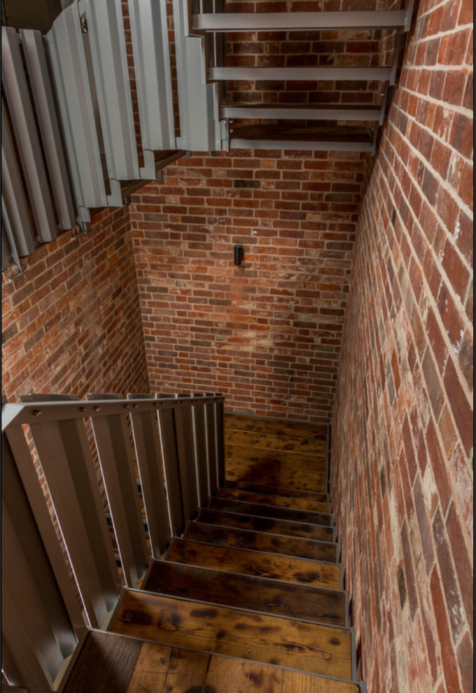 This is an example of a mid-sized contemporary wood u-shaped staircase in Other with open risers, metal railing and brick walls.