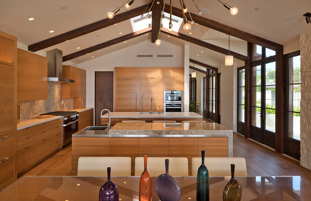 Inspiration for a large contemporary l-shaped eat-in kitchen in Los Angeles with flat-panel cabinets, multiple islands, medium wood cabinets, beige splashback, stone slab splashback, stainless steel appliances, medium hardwood floors, an integrated sink, stainless steel benchtops, beige benchtop and brown floor.