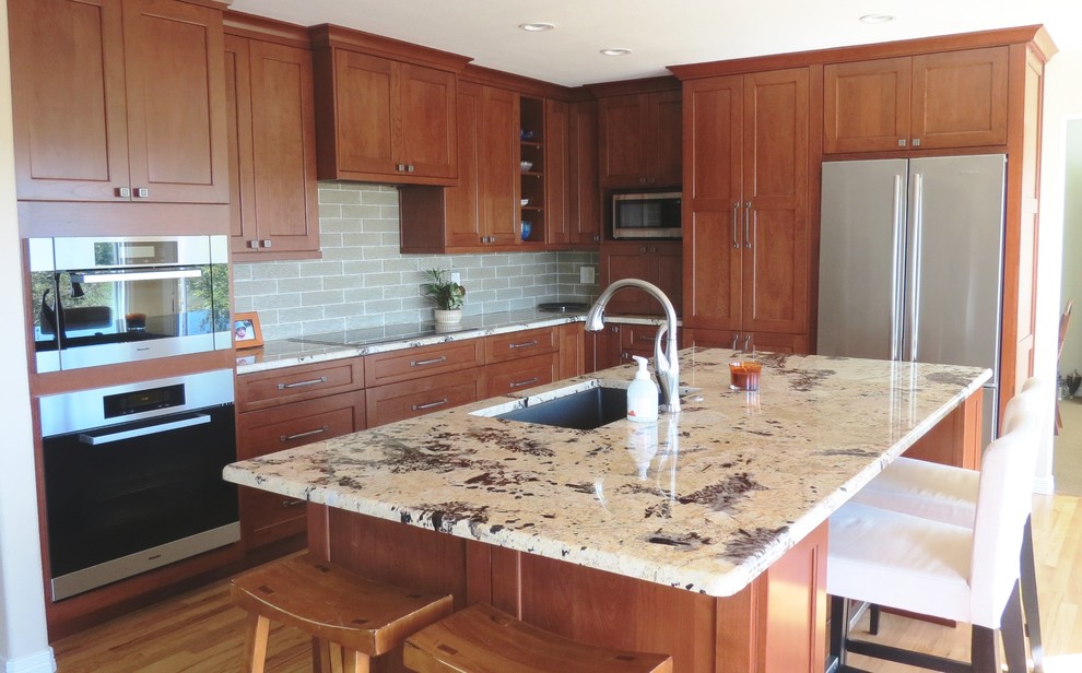 Open concept kitchen - mid-sized transitional l-shaped light wood floor open concept kitchen idea in Denver with a single-bowl sink, recessed-panel cabinets, medium tone wood cabinets, granite countertops, green backsplash, glass tile backsplash, stainless steel appliances and an island