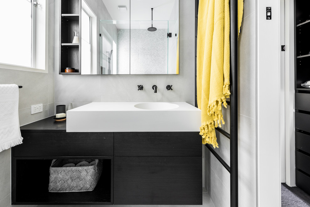 Inspiration for a mid-sized contemporary master wet room bathroom in Melbourne with flat-panel cabinets, dark wood cabinets, a drop-in tub, a one-piece toilet, gray tile, porcelain tile, grey walls, porcelain floors, an integrated sink, solid surface benchtops, grey floor and a hinged shower door.