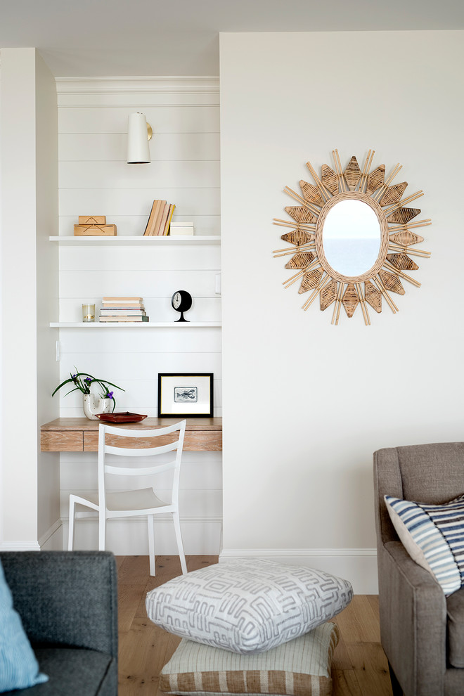 Small beach style study room in Portland Maine with white walls, light hardwood floors, a built-in desk and beige floor.