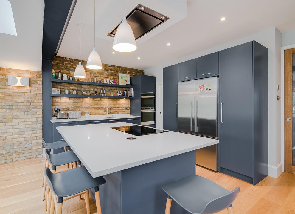 This is an example of a mid-sized contemporary l-shaped kitchen in London with flat-panel cabinets, solid surface benchtops, white splashback, stainless steel appliances, with island, an undermount sink, blue cabinets, brick splashback, medium hardwood floors, brown floor and white benchtop.