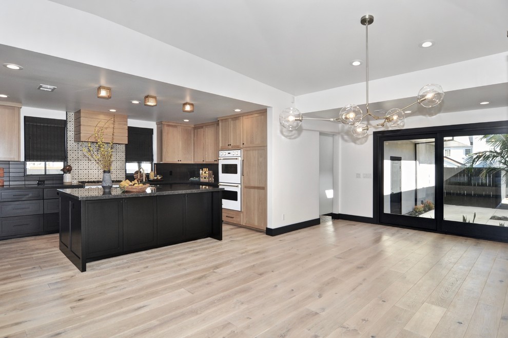 This is an example of a large transitional u-shaped eat-in kitchen in Orange County with a single-bowl sink, shaker cabinets, light wood cabinets, marble benchtops, black splashback, cement tile splashback, white appliances, light hardwood floors, with island, beige floor and black benchtop.