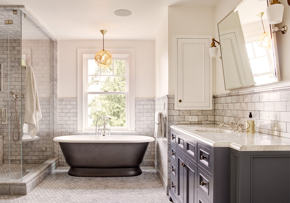 This is an example of a traditional master bathroom in Seattle with recessed-panel cabinets, grey cabinets, a freestanding tub, white tile, marble, white walls, marble floors, an undermount sink and white floor.