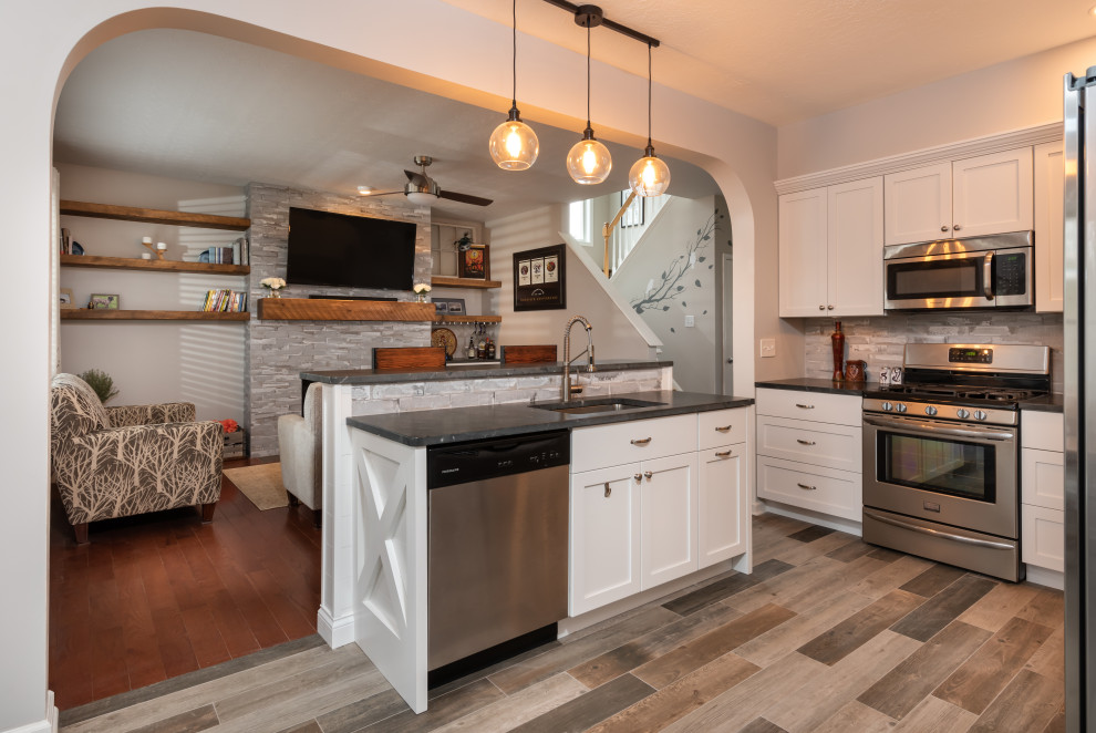 Mid-sized mountain style l-shaped porcelain tile and gray floor open concept kitchen photo with an undermount sink, shaker cabinets, white cabinets, granite countertops, gray backsplash, brick backsplash, stainless steel appliances, an island and black countertops