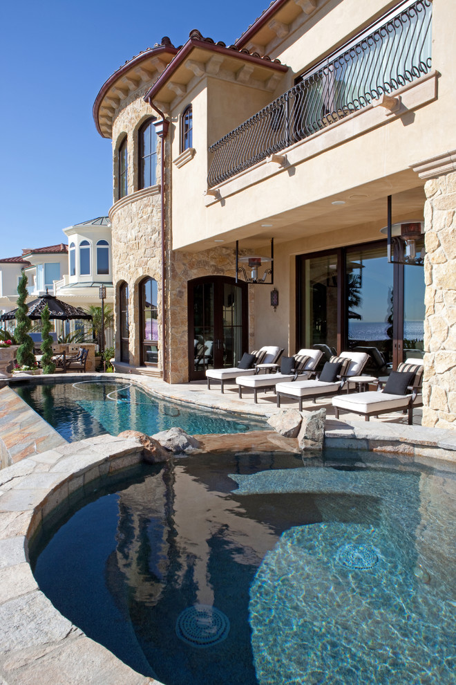 Mid-sized mediterranean backyard custom-shaped pool in San Diego with natural stone pavers.