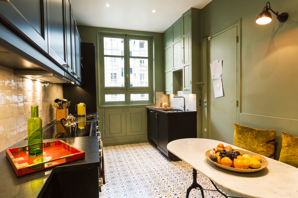 Photo of a large industrial single-wall eat-in kitchen in Paris with an undermount sink, cement tiles, recessed-panel cabinets, black cabinets, beige splashback, mosaic tile splashback, black appliances, no island, pink floor and black benchtop.