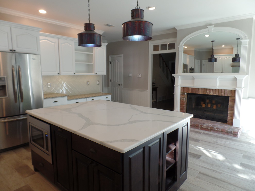 Photo of a large traditional l-shaped eat-in kitchen in Other with an undermount sink, raised-panel cabinets, white cabinets, granite benchtops, white splashback, glass tile splashback, stainless steel appliances, porcelain floors, with island and grey floor.