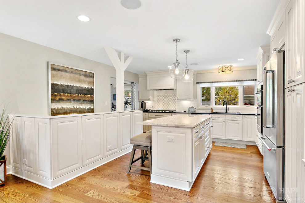 Large transitional l-shaped kitchen photo in Chicago with white cabinets, white backsplash, an island and black countertops
