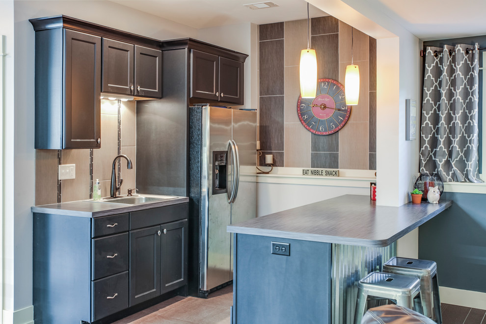 This is an example of an arts and crafts galley wet bar in Grand Rapids with a drop-in sink, recessed-panel cabinets, dark wood cabinets, laminate benchtops, beige splashback, ceramic splashback, vinyl floors, grey floor and grey benchtop.