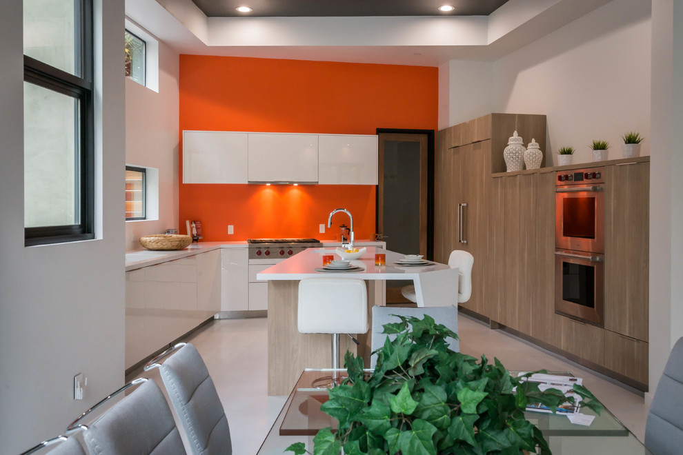 This is an example of a large modern u-shaped eat-in kitchen in Los Angeles with an undermount sink, flat-panel cabinets, distressed cabinets, quartz benchtops, orange splashback, glass sheet splashback, stainless steel appliances, porcelain floors, with island, grey floor and white benchtop.