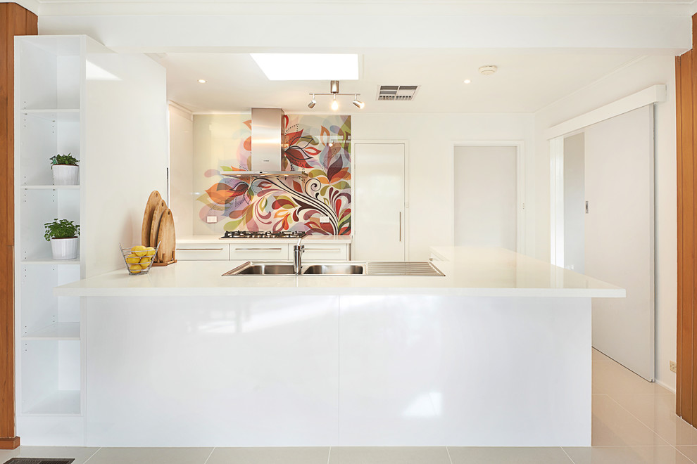 Design ideas for a mid-sized contemporary galley open plan kitchen in Melbourne with a double-bowl sink, flat-panel cabinets, white cabinets, quartz benchtops, multi-coloured splashback, glass sheet splashback, stainless steel appliances, porcelain floors and a peninsula.