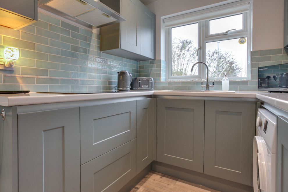 Inspiration for a small contemporary u-shaped enclosed kitchen in Essex with a single-bowl sink, shaker cabinets, blue cabinets, laminate countertops, blue splashback, ceramic splashback, black appliances, laminate floors, no island and white worktops.