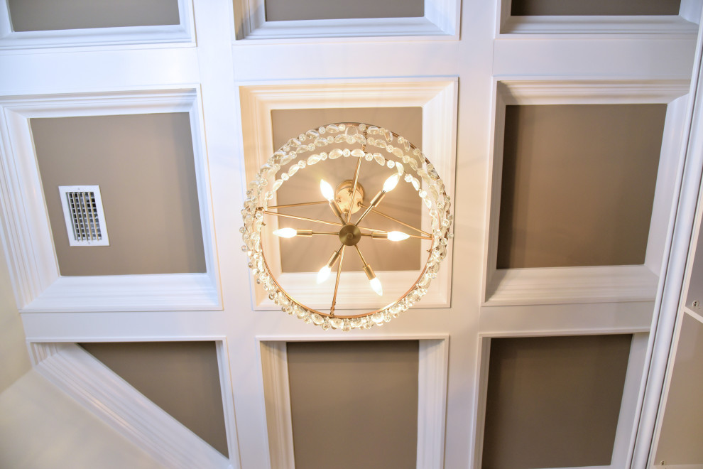 This is an example of a mid-sized transitional gender-neutral storage and wardrobe in Jacksonville with raised-panel cabinets, dark hardwood floors, brown floor and coffered.